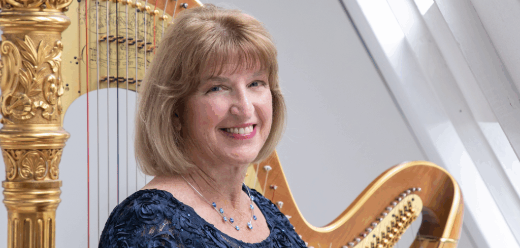 Barbara Lepke-Sims stands with her harp in front of a white background