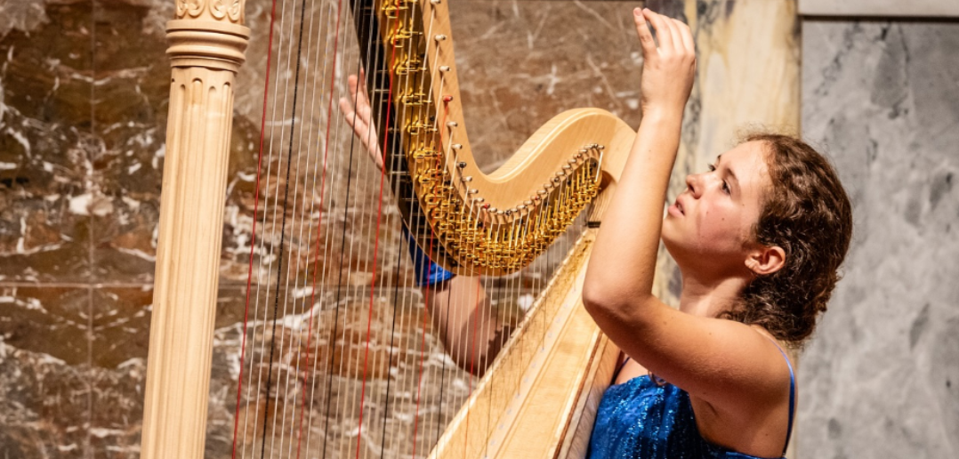 Zoé Buyck playing a harp with a marble wall in the background