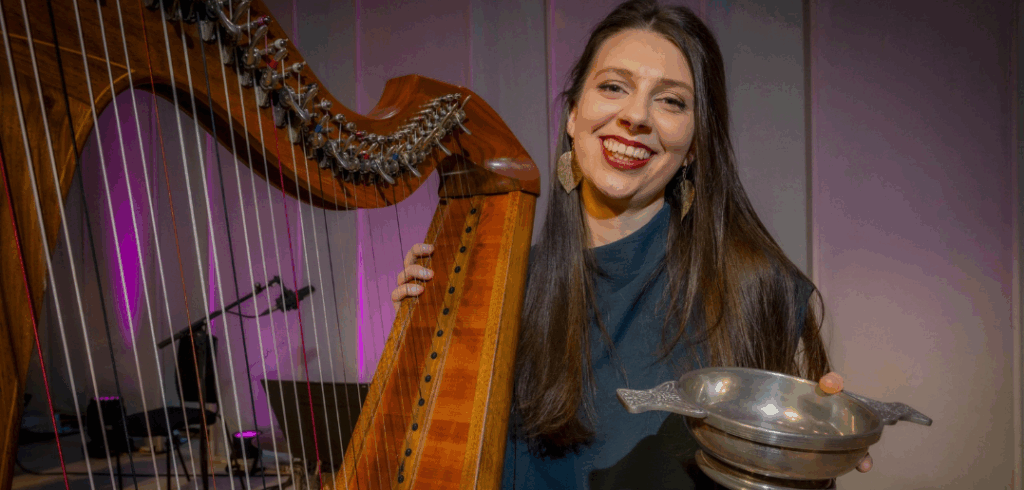 Rachel_Groves_2026_BBC_Radio_Scotland_Young_Traditional_Musician_pc_Alan_Peebles Rachel Groves sitting behind her lever harp with a trophy