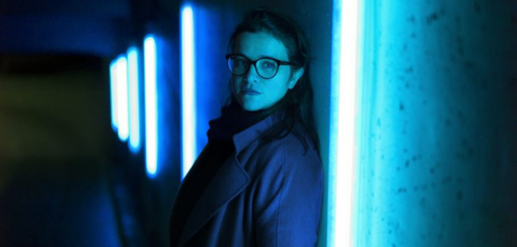 Sunniva_Rødland_pc-Bjørn_Wad Sunniva Rødland stands in a dark hallway with dramatic blue lighting
