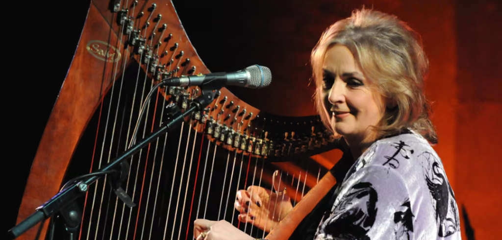 Moya Brennan performs on a lever harp, with her face turned towards a microphone positioned for singing