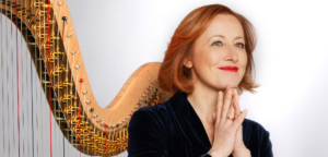 Anne-Sophie Bertrand stands in front of her harp and looks upward, smiling