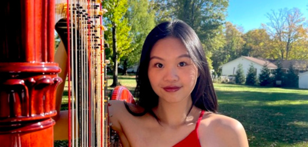 Ashley Lim stands beside a red harp wearing a red dress