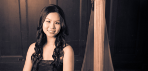 Joy Yeh sits beside her harp smiling