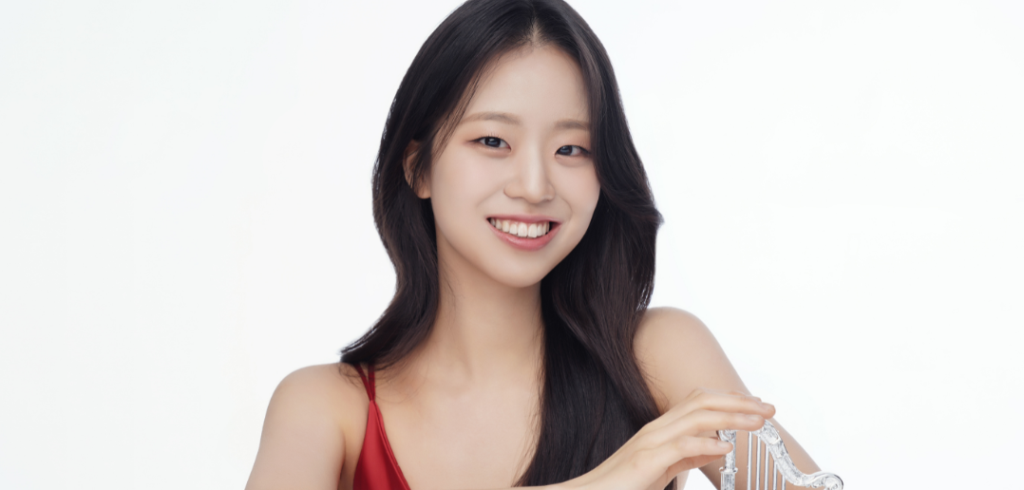 Subin Lee smiles while resting her hand on a miniature crystal harp against a light gray backdrop
