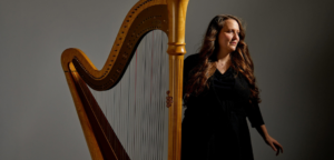 Anna Hagen stands beside her harp against a gray gradient background