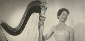 Black-and-white image of Sheila Larchet Cuthbert with her hand on an Erard harp